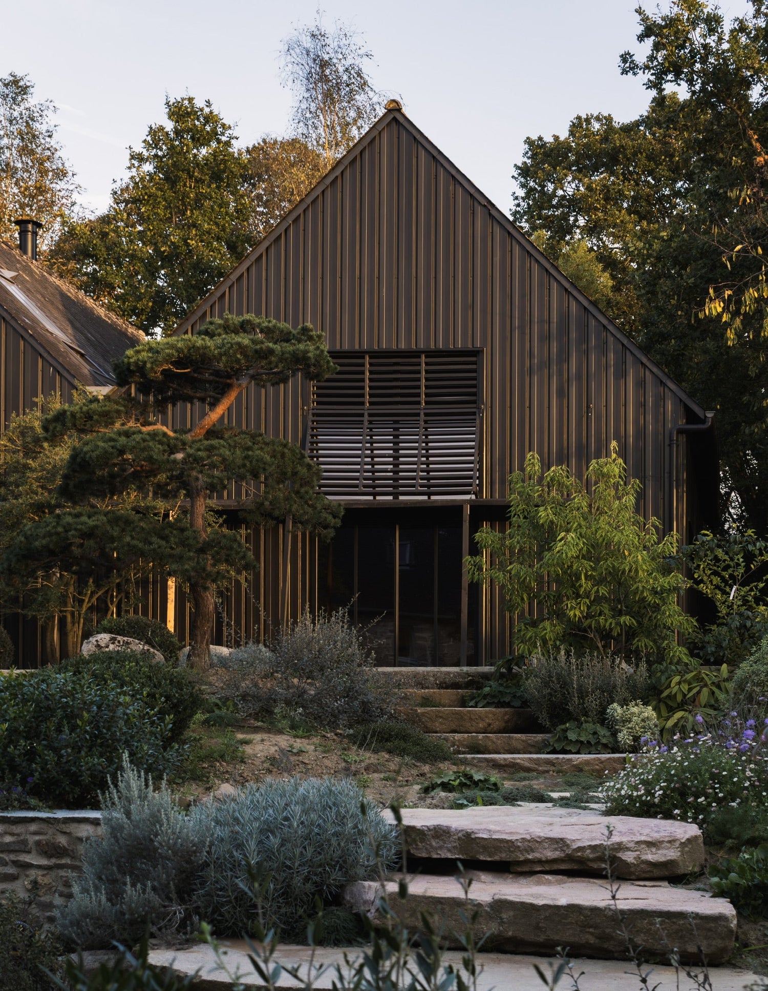 Vue sur le hangar et les escaliers y menant à travers le jardin et les terrasses de l'Arbre qui marche