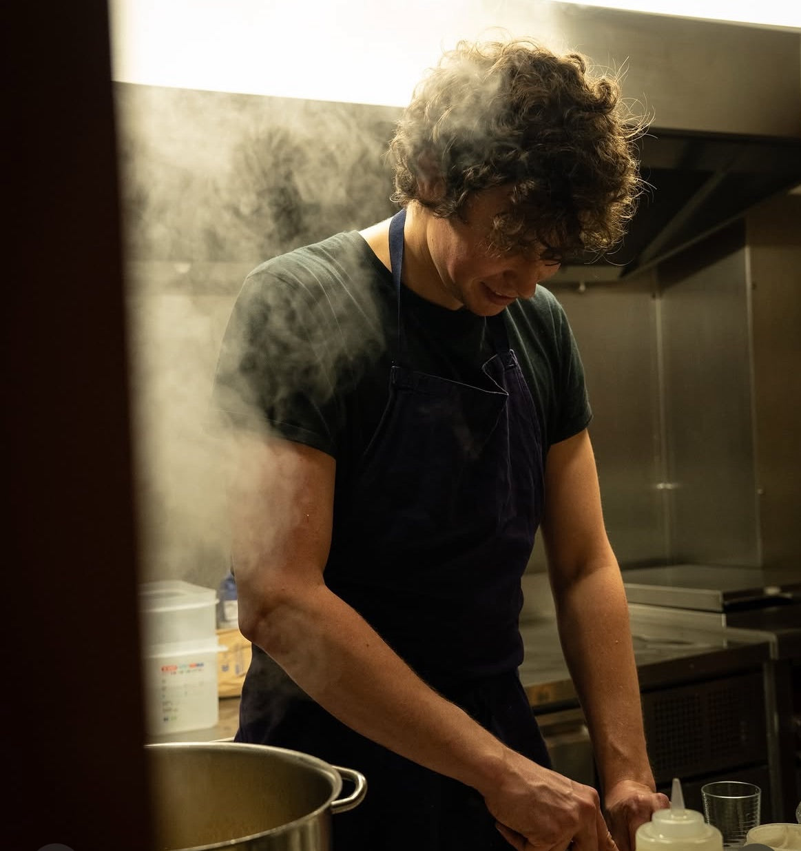 Jean-Victor un cuisinier de l'Arbre qui marche s'affaire dans la vapeur des fourneaux en cuisine. Photo de Justine Nerini