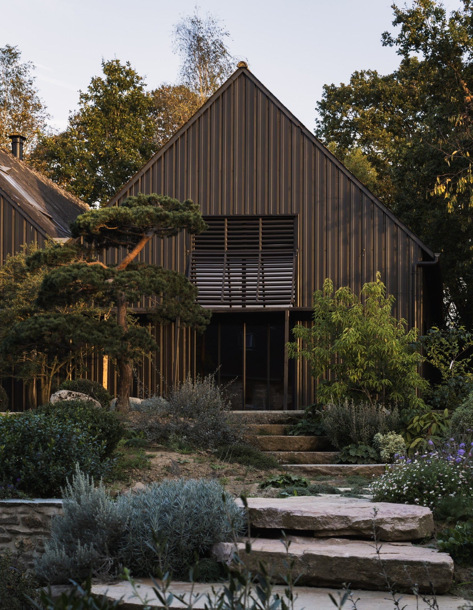 Vue sur le hangar et les escaliers y menant à travers le jardin et les terrasses de l'Arbre qui marche